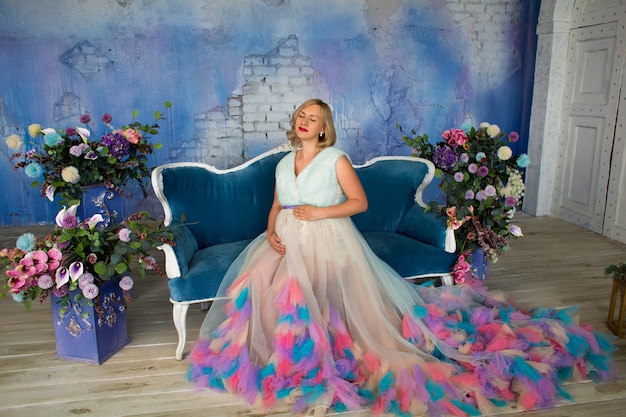 Photo beautiful pregnant woman is sitting on the sofa in loft studio among flowers with her eyes closed