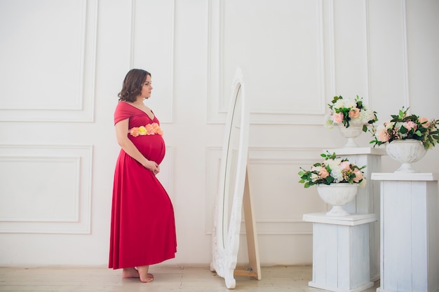 Beautiful pregnant woman looking in mirror in light room