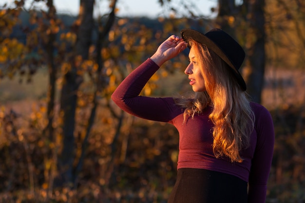 Beautiful pregnant woman looks to sun, holds hat with hand. Relaxing outside