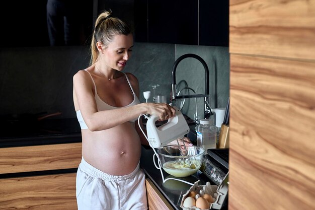 Beautiful pregnant woman making fruits smoothies with blender H