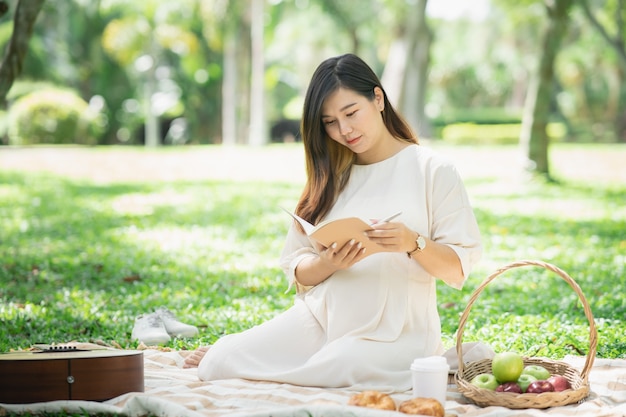 The beautiful pregnant woman on picnic and reading a notebook in the garden