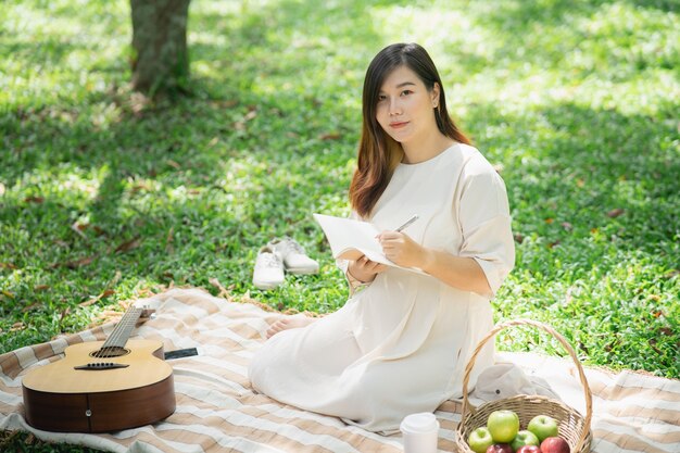 Красивая беременная женщина на пикнике и читает тетрадь в саду