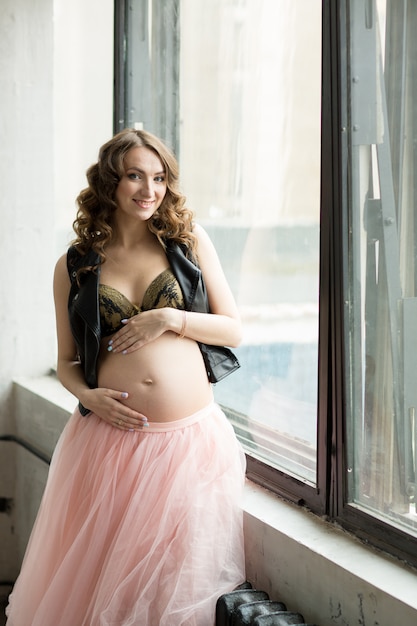 Photo beautiful pregnant woman in pink skirt posing by window