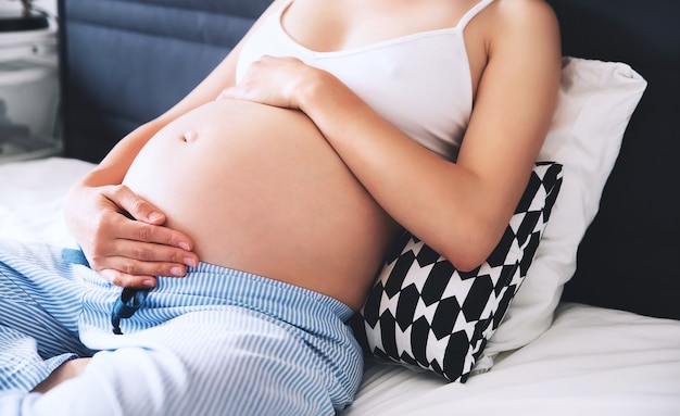 Фото Красивая беременная женщина сидит на кровати и держит руки на животе дома концепция беременности