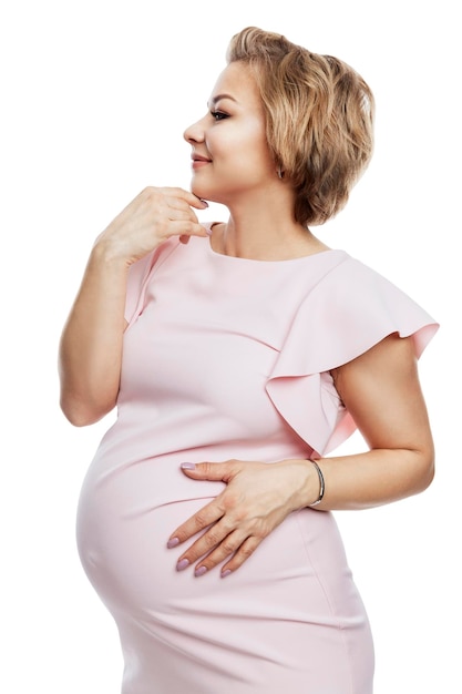 Beautiful pregnant woman. Smiling blonde in a pink dress. Happy motherhood, love and tenderness. Profile view. Isolated on white background. Vertical.