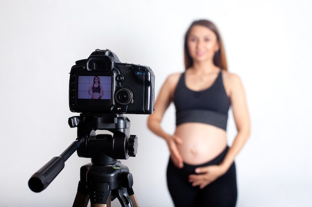 A beautiful pregnant woman in a sports uniform shoots a video about sports during pregnancy