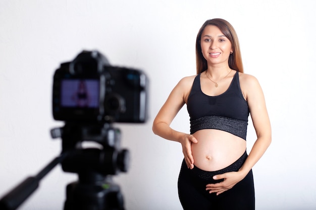 A beautiful pregnant woman in a sports uniform shoots a video about sports during pregnancy