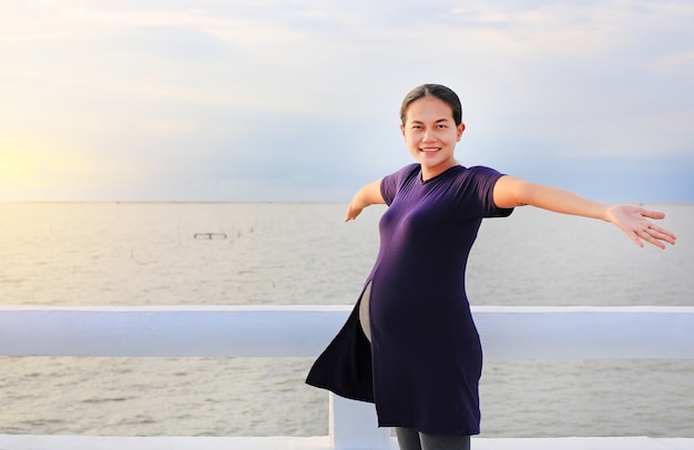 Beautiful pregnant woman standing on seashore with open arms.