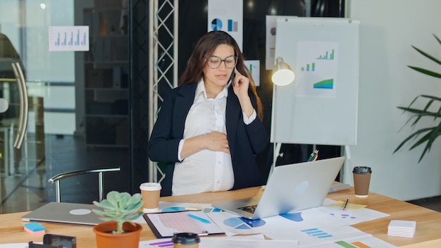 A beautiful pregnant woman talking on a cell phone sitting at a table