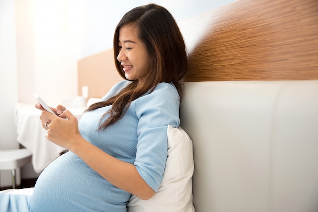 Beautiful pregnant woman using mobile phone in her bedroom