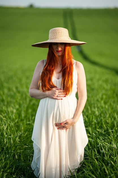 Beautiful pregnant woman in white dress walking in the green field