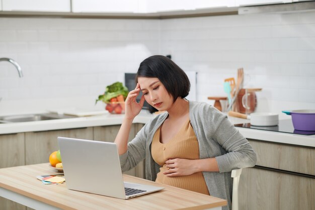 写真 キッチンでラップトップを持つ美しい妊婦