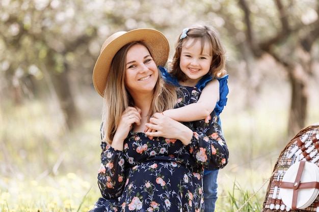 Beautiful pregnant woman with little daughter playing on a picnic in a blooming spring garden