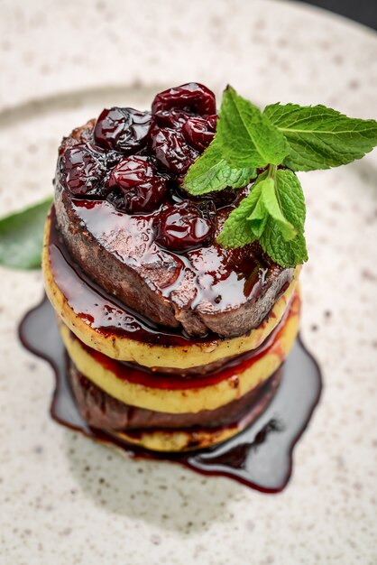 a beautiful presentation of fried meat with an apple, rosemary, with cherry sauce