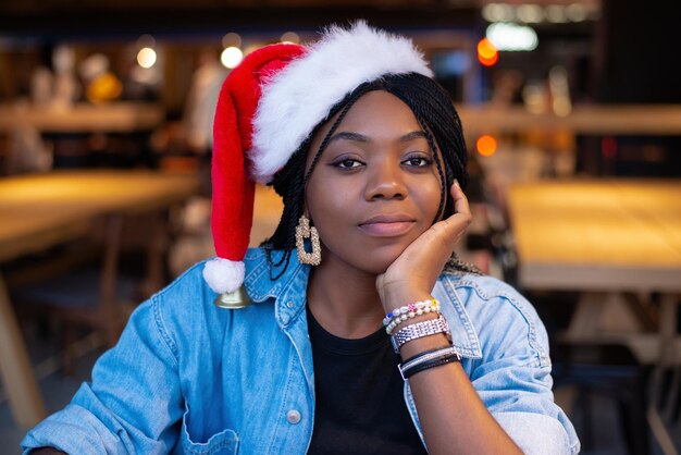 A beautiful pretty brunette with Afro pigtails and dark skin in a Santa Claus hat