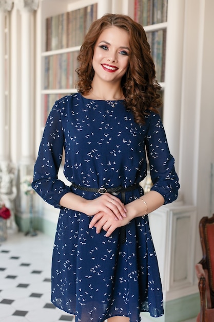 Beautiful pretty girl in blue sheath cocktail dress posing in luxury library interior