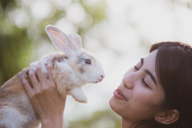 Beautiful pretty portrait of young Asian woman person with cute rabbit in pet and animal care concept happy female holding bunny at nature outdoor field with friendship easter concept