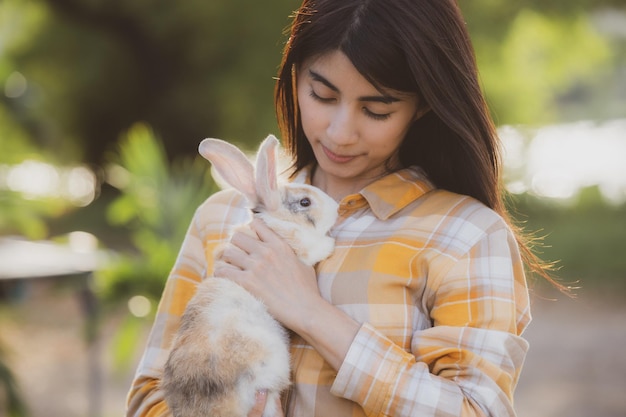 Beautiful pretty portrait of young Asian woman person with cute rabbit in pet and animal care concept happy female holding bunny at nature outdoor field with friendship easter concept