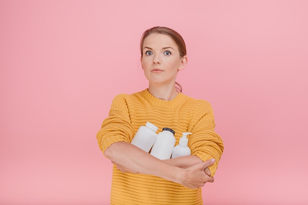 Bella donna graziosa che tiene in mano una bottiglia di pillole mediche o vitamine vestita casualmente con espressione dubbiosa