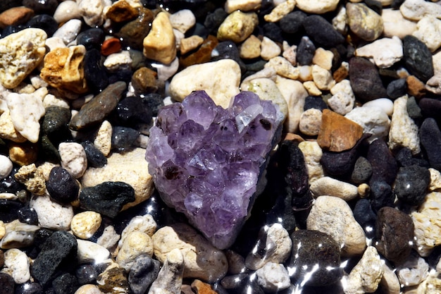 Bellissimi cristalli di ametista viola su ciottoli bagnati in riva al mare druse di ametista viola brillante a forma di cuore sullo sfondo del mare