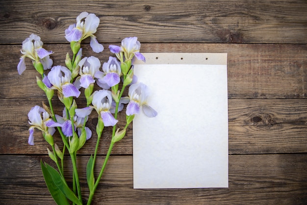 Beautiful purple flowers irises, a sheet of paper on a wooden background