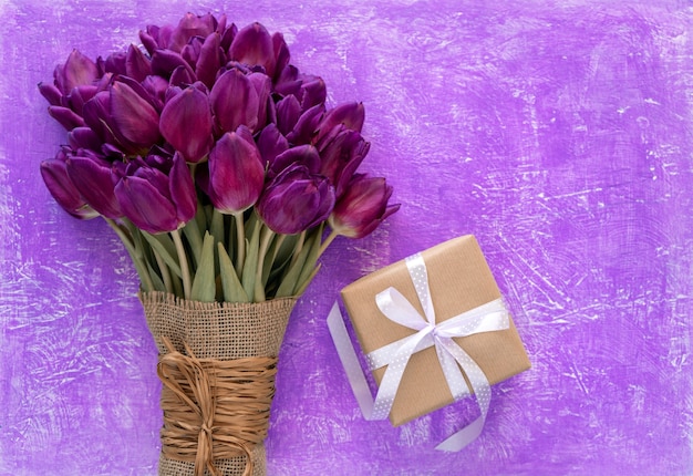 紫色のテーブルの上の美しい紫色のチューリップの花束とギフトボックス。