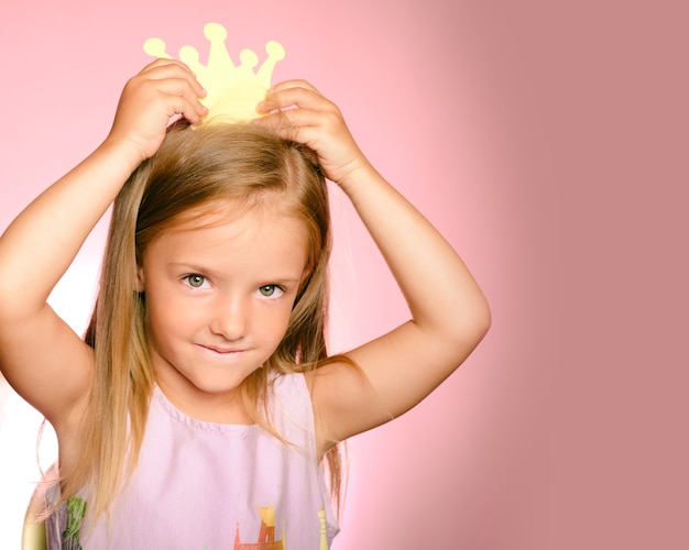 Beautiful queen in gold crown. Little princess girl in yellow crown and beautiful dress on pink background.