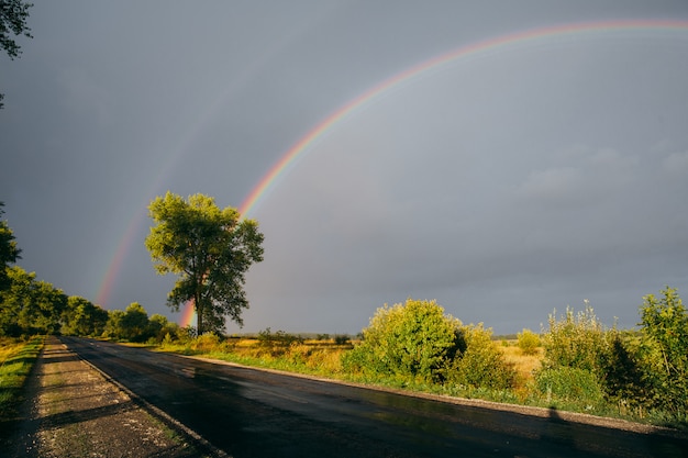 A beautiful rainbow in the grey sky shining over the fields