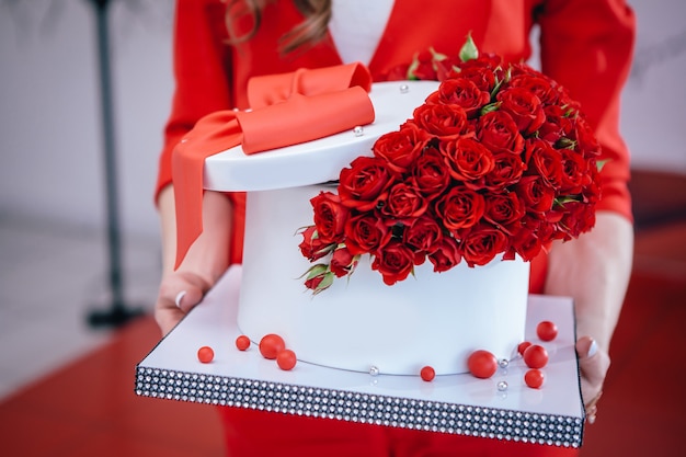 Beautiful red cake with bow and roses held in hands for birthday.