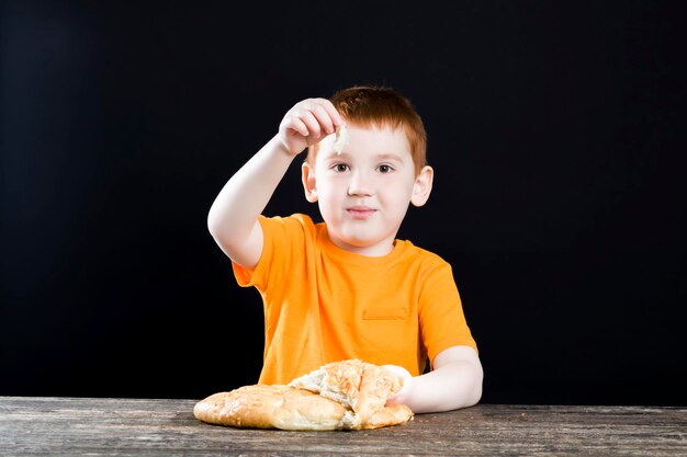 おいしいパンのパンを持つ美しい赤い髪の少年、少年は喜びでパンを食べる、小麦粉から作られたおいしい食べ物