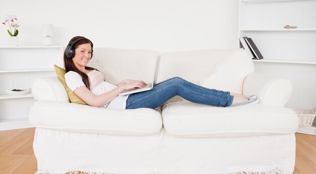 Beautiful red-haired female listening to music with headphones while relaxing with her laptop