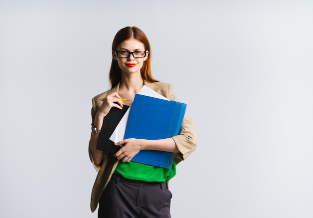 Beautiful red-haired girl with glasses is holding a folder in her hands and looking at the camera, isolated