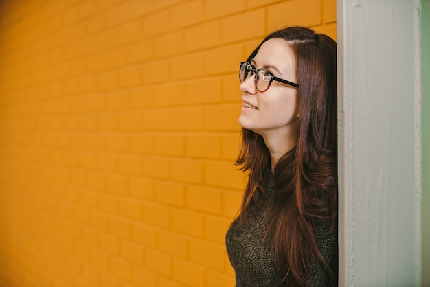 Beautiful red-haired woman in glasses on yellow brick wall