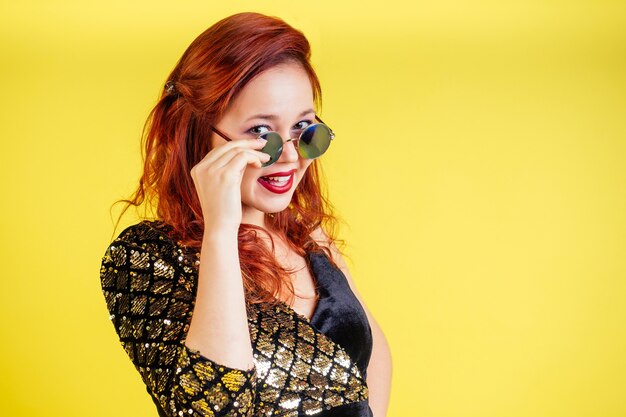 Beautiful red-haired woman in sunglasses dancing dance in yellow background in studio