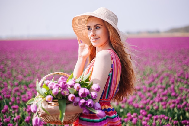 Beautiful red haired woman wearing striped dress and holding bouquet of tulips flowers in basket