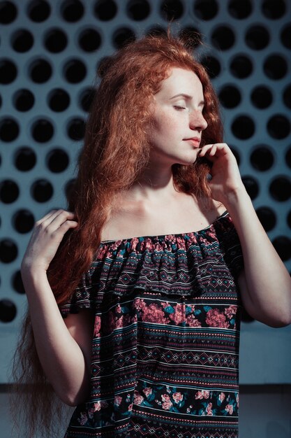 Beautiful red head model with long lush hair in rays of sun at the street