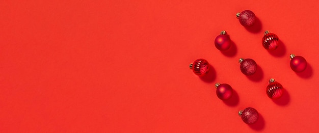 美しい赤い小さな装飾的なボールが赤い背景に散らばっています。上面図、フラットレイ。バナー。
