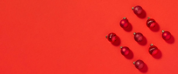 Beautiful red small decorative balls are scattered on a red background. Top view, flat lay. Banner.