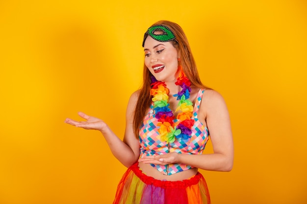 Beautiful redhaired Brazilian girl in carnival clothes presenting something to the left