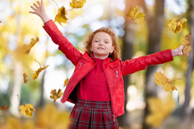 Photo beautiful redhaired girl in the autumn park scatters maple leaves