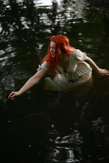 Beautiful redhaired girl in a white dress in the lake