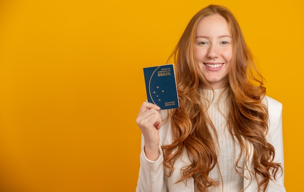 Beautiful redhead curly-haired girl in travel. Next trip. Girl holding Brazilian passport. On yellow.