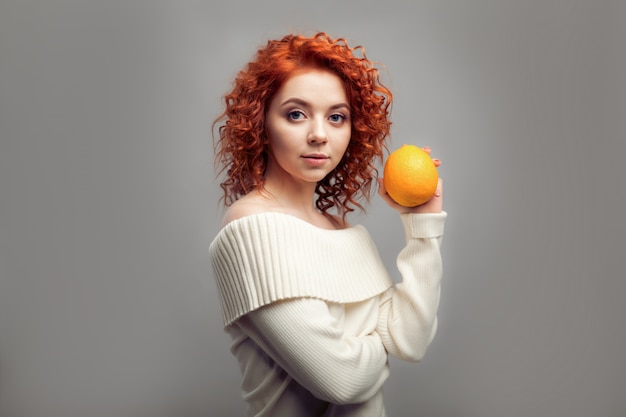 Beautiful redhead curly woman eating Orange