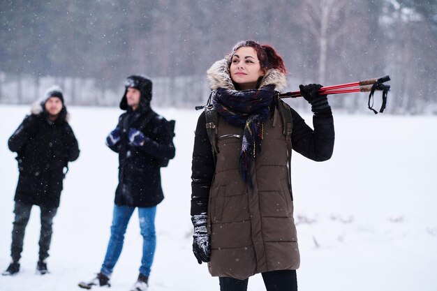 Beautiful redhead girl posing in a camera stand next to her friends in the snowy forest