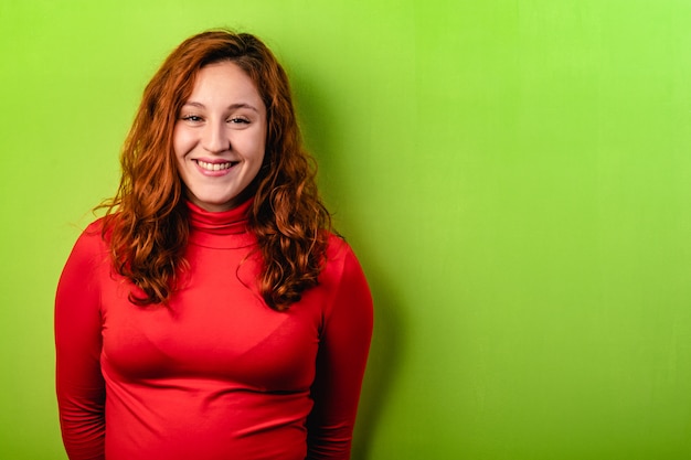 Beautiful redhead girl with red shirt and green wall. Copy space for text
