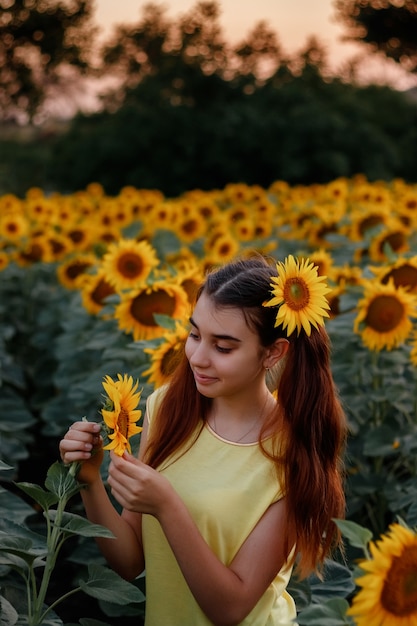 Beautiful redhead girl in a yellow tshirt on a field with sunflowers at sunset