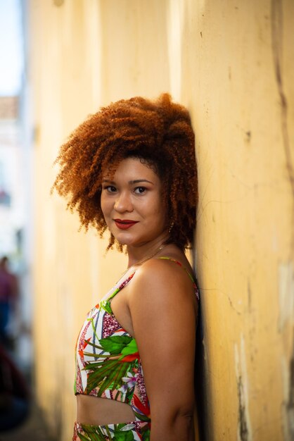 Photo beautiful redhead woman looking at camera leaning against an old lightcolored wall of a street happy person traveling