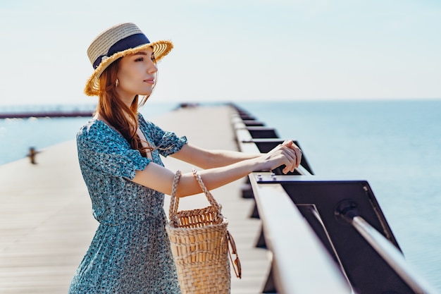 Photo beautiful redhead woman posing at sunny day walks along the pier near the sea girl wearing fashionab...