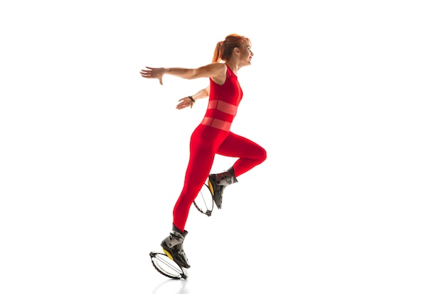 Beautiful redhead woman in a red sportswear jumping in a kangoo jumps shoes isolated on white studio