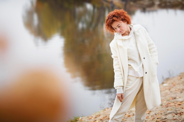 Beautiful redhead woman walking and relaxing outdoors in autumn around lake